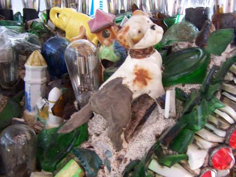 A ceramic dog figure with brown spots sitting among glass bottles and debris
