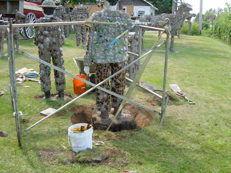 Camouflage-covered human figures standing on a grassy lawn near a metal frame