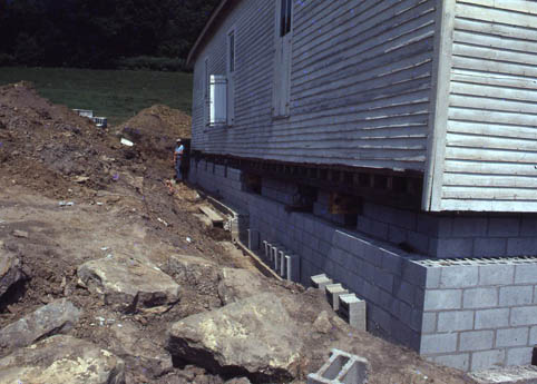 A house raised on a new cinder block foundation beside a dirt excavation