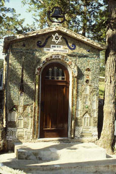 Small mosaic-tiled grotto building with arched wooden door and Star of David