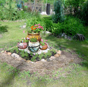 A garden bed with stacked ceramic pots and flowers bordered by stones