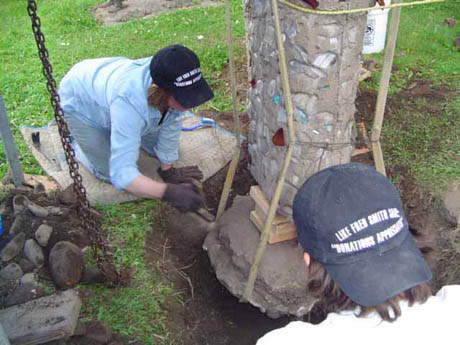 Two people in black caps working on a concrete pillar outdoors