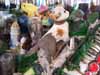 A blurry folk-art figure in a hat surrounded by greenery and decorative objects