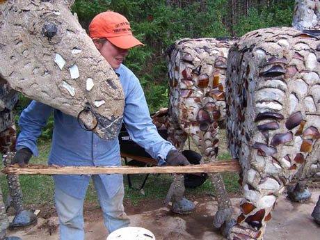 Person in orange cap assembling shell-covered concrete animal sculptures