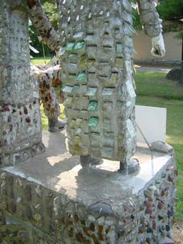 Concrete statue of a figure embedded with bottle caps and glass on a pedestal