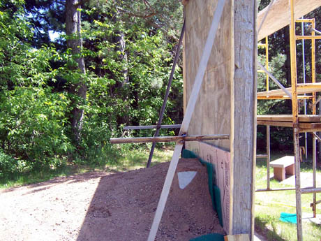 A wooden wall under construction beside scaffolding and a dirt pile
