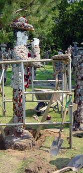 A shell-covered concrete pillar topped by a white figure within a wooden frame