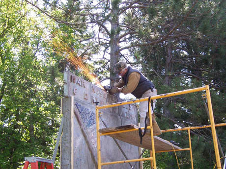 Man on yellow scaffolding grinding a concrete wall with sparks flying