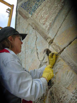 A person in yellow gloves using a tool on a textured wall