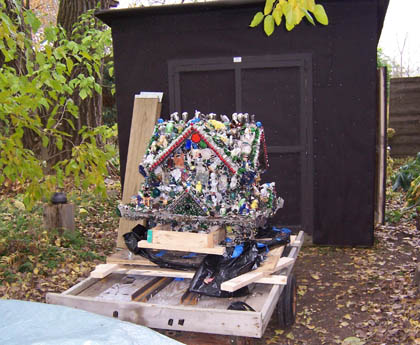 Bottle-cap-covered house sculpture on a wooden cart