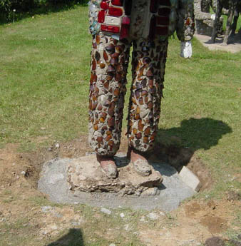 Mosaic-tiled figure's legs and feet standing on a concrete base