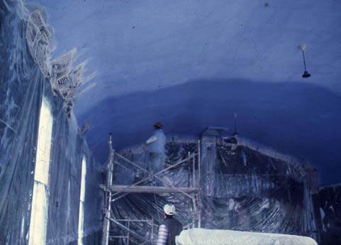 Two workers on scaffolding inside a blue-ceilinged painted interior