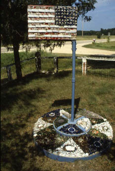 Weathered painted American flag sign on a pole with a circular shell mosaic base