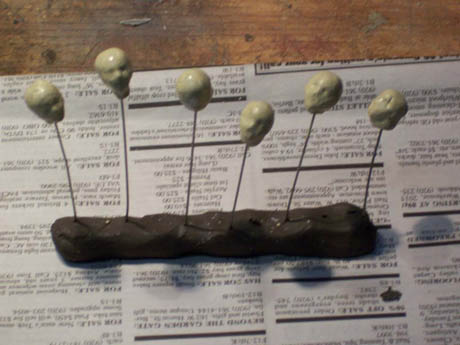 A dark sculpted figure with six wire stems topped by pale balls