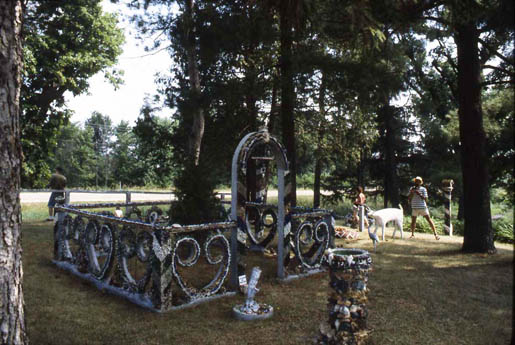 Ornamental metal fence and arch in a wooded yard with a person and dog