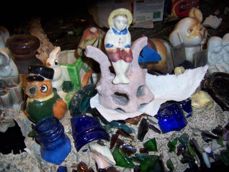An arrangement of ceramic figures, animal sculptures, and broken glass on sand