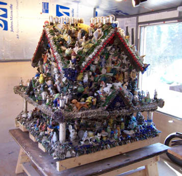 A house-shaped folk-art structure densely covered with figurines on a wooden table