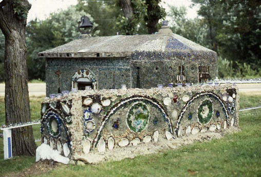 Small mosaic-covered building fronted by a shell-and-tile wall with arches