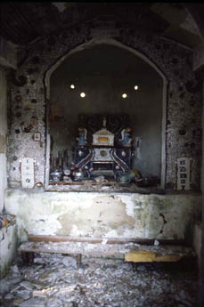 An arched grotto niche with statues on a shelf above a debris-covered floor