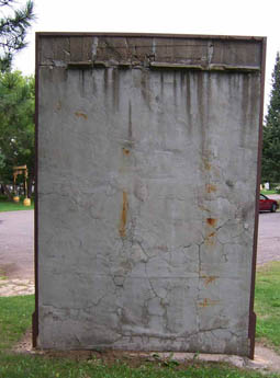 Weathered gray concrete wall with rusty metal frame standing on grass