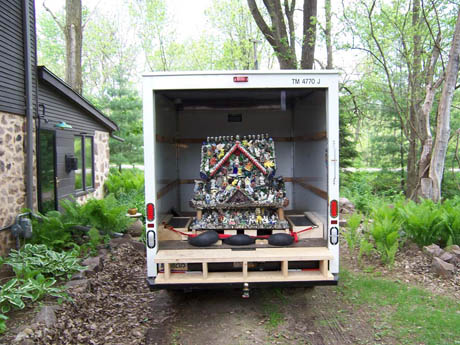 A colorful assemblage sculpture loaded in the open back of a white truck