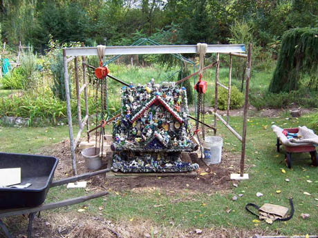 A small ornamented house structure framed by a metal rig with pulleys and buckets