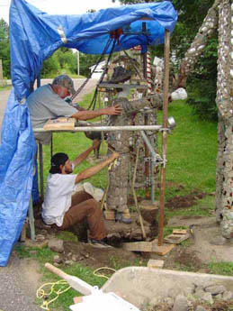 Two people working on a concrete structure under a blue tarp