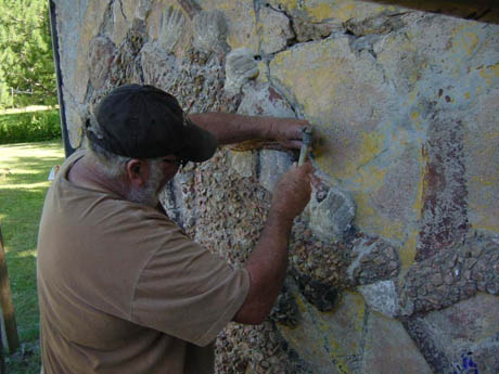 Man in cap and tan shirt working on textured stone wall