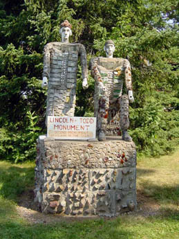 Two mosaic-covered human figures standing on a stone pedestal with a sign
