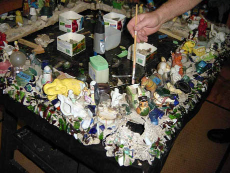 Table surface encrusted with ceramic figurines and a hand holding a paintbrush