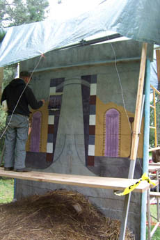 A man working on a painted concrete mural structure under a tarp