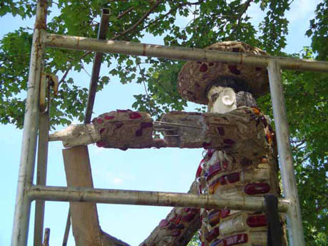 Patchwork figure in a wide-brimmed hat standing within a metal frame